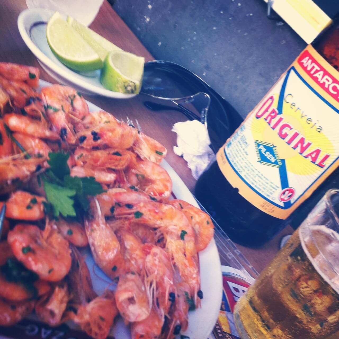 Petiscos e garrafas de cerveja são servidas em mesas de madeira na calçada de boteco tradicional carioca.
