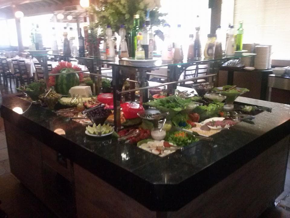 Carnes assadas na brasa e buffet de saladas e pratos quentes, em casa com decoração rústica e espaço infantil.