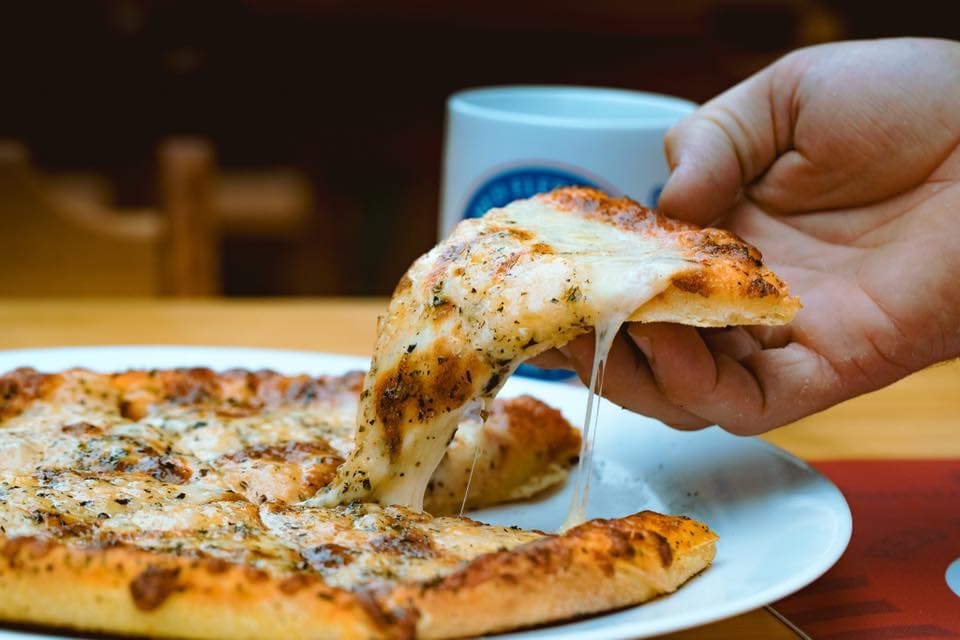Cantina no estilo fast-food com mesas externas e cervejas serve pizzas diversificadas com opções inesperadas.