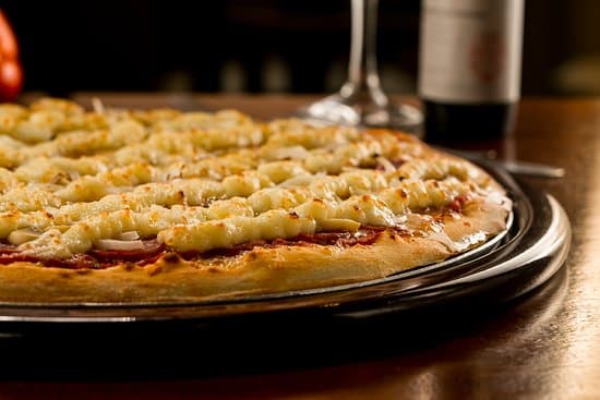 Pizzas assadas na hora, além de refrigerantes e cervejas, em loja com mesinhas na praça de alimentação.