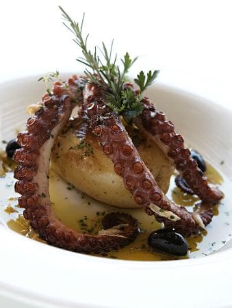 Gastronomia internacional com influência portuguesa, vinhos e drinques, clima moderno com vista para o mar.