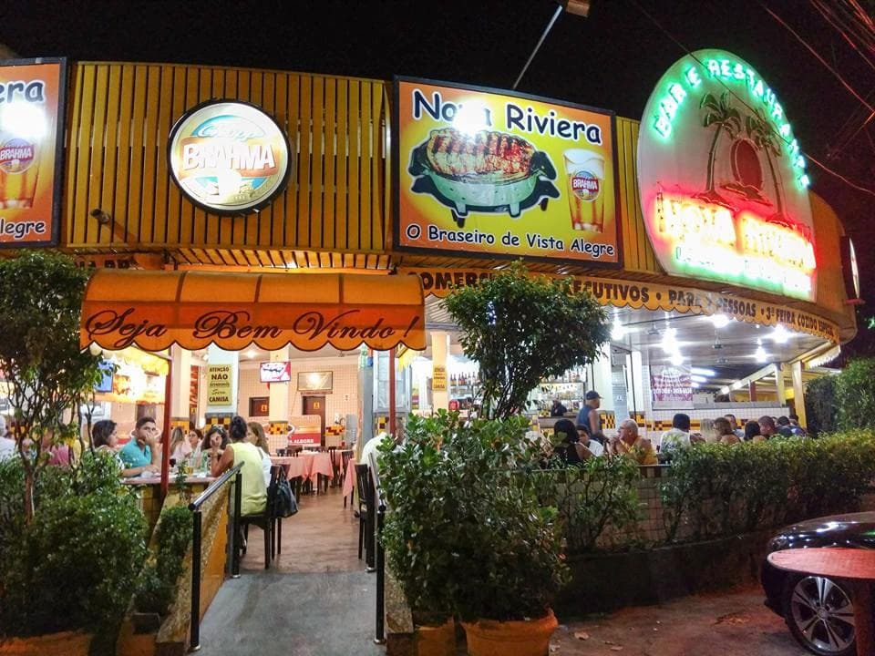 Restaurante com destaque à picanha assada em braseiro na mesa, farofa, vinagrete e bebidas, em clima simples.