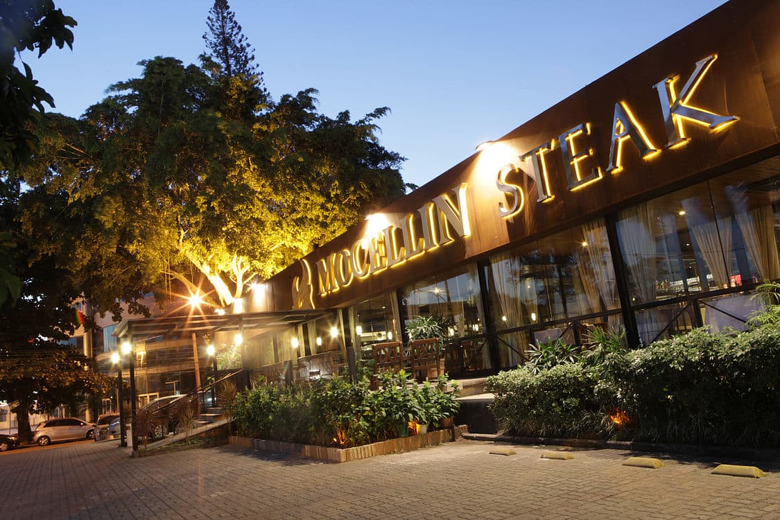 Steakhouse com diversos tipos de carne e buffet variado de saladas e pratos quentes em ambiente elegante.